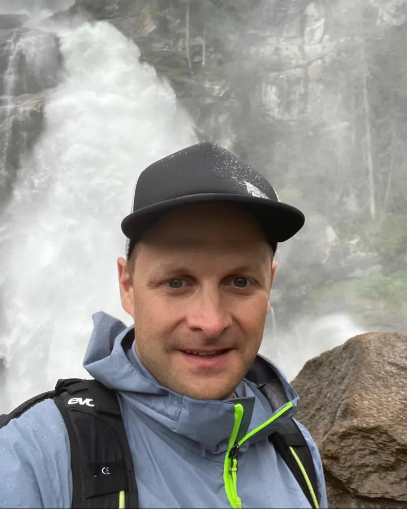 Frederik Leikop mit Kappe und Regenjacke vor einem Wasserfall